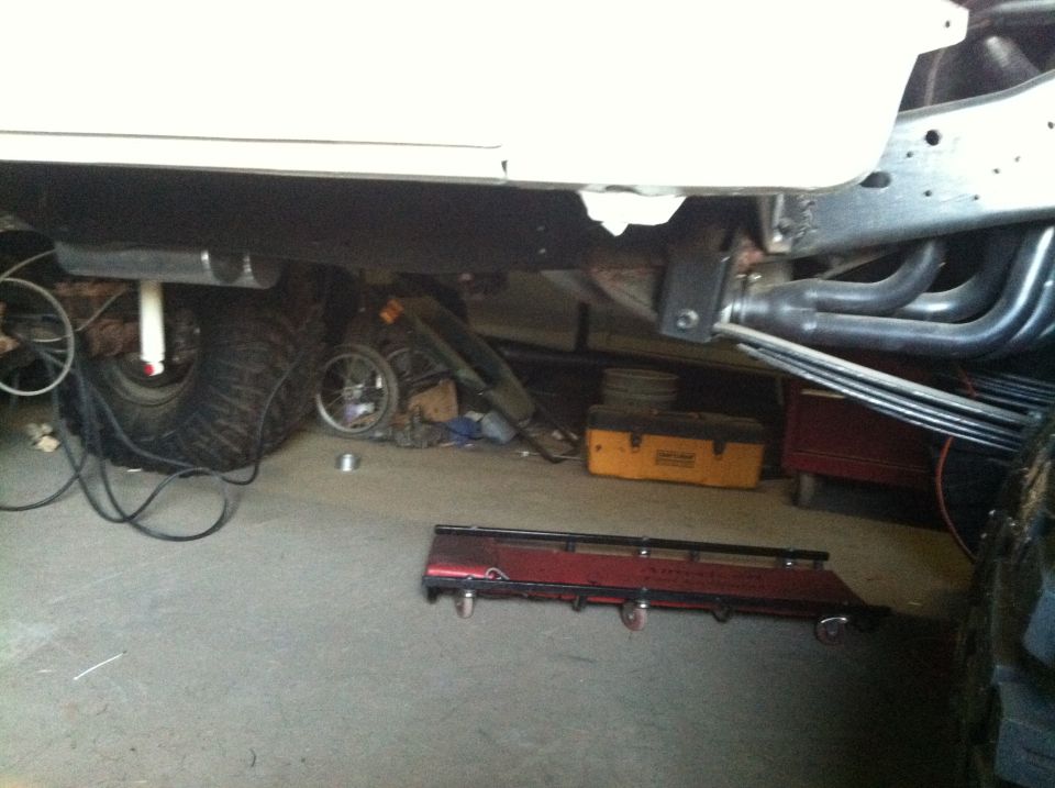 Underside of a vehicle showing exhaust, suspension, and tire in a garage.
