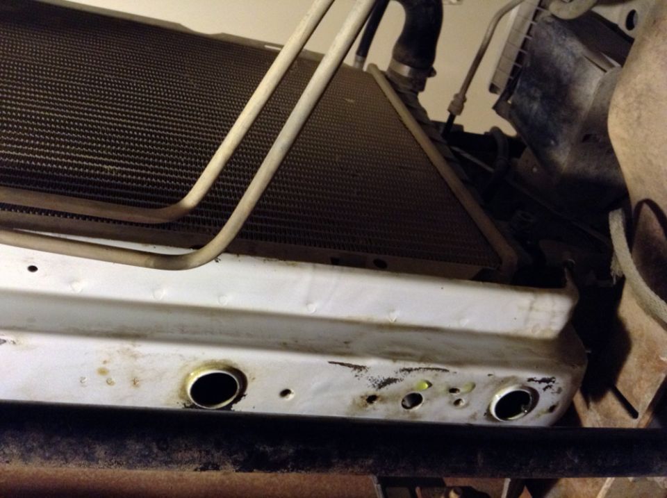 Close-up of vehicle radiator and white mounting bracket with circular openings.