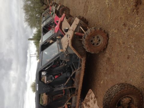 1996 Ford Bronco - Several off-road vehicles are parked in a muddy outdoor area under a cloudy sky.