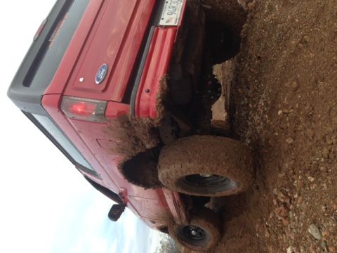 1996 Ford Bronco - This red Ford Bronco is stuck in the mud, showing its rear end and tires covered in dirt.