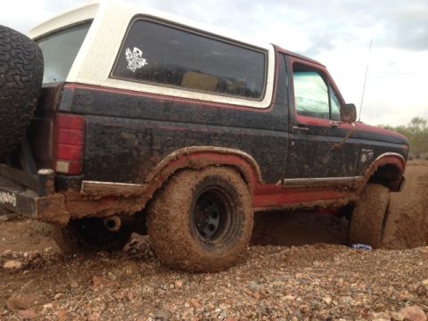 1996 Ford Bronco - A muddy Ford Bronco is stuck in the dirt, with a spare tire mounted on the rear.