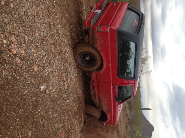 Red 1996 Ford Bronco stuck in dirt with black wheels and mud splatters