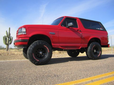 1996 Ford Bronco - A red Ford Bronco SUV is seen from a 3/4 front angle on a desert road with a saguaro cactus nearby.