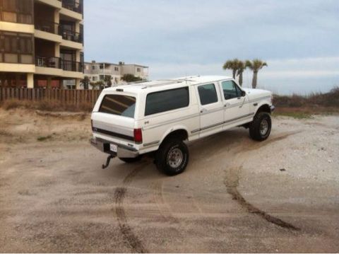 1995 Ford Bronco - Extended cab pickup truck with large tires parked on a sandy lot near the coast.