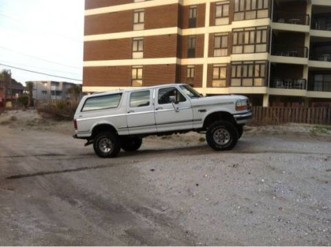 1995 Ford Bronco - This 1995 Ford Bronco extended cab pickup truck is seen from the side, parked on a sandy surface in front of a building.