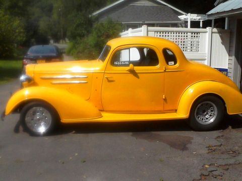 1935 Chevrolet New - A bright yellow 1935 Chevrolet coupe is parked outdoors, showing its classic side profile.