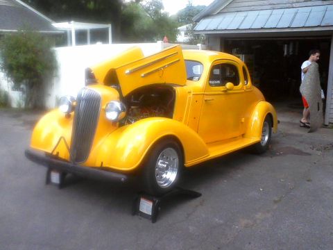 1935 Chevrolet New - A bright yellow 1935 Chevrolet coupe is shown with its hood open, revealing the engine bay.