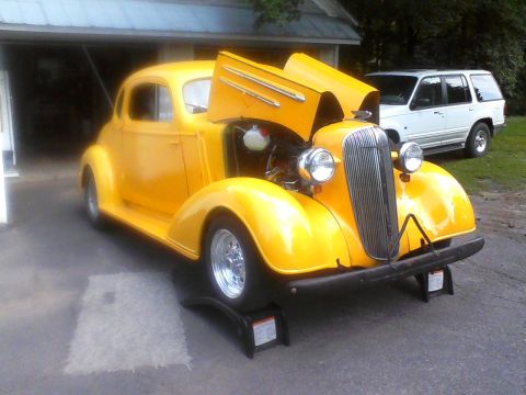 1935 Chevrolet New - Yellow 1935 Chevrolet New coupe hot rod with hood open, parked in front of a garage.