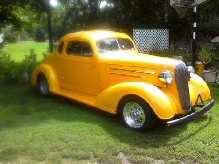1935 Chevrolet New - A bright yellow coupe hot rod sits on a grassy lawn, with trees and a basketball hoop visible.