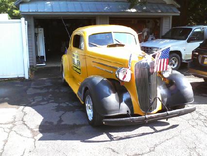 1935 Chevrolet New - A yellow 1935 Chevrolet coupe is parked in front of a garage, with an American flag attached to its grille.