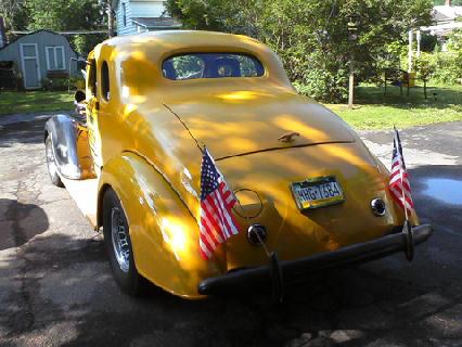 1935 Chevrolet New - Rear view of a yellow 1935 Chevrolet New coupe, adorned with two American flags and a license plate reading 'WHG-7584'.