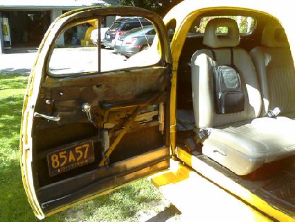 1935 Chevrolet New - The interior of a yellow vehicle is shown with the driver's side door open, revealing the seats and a license plate.