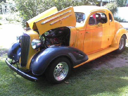 1935 Chevrolet New - A yellow 1935 Chevrolet New coupe is shown with its hood open, revealing the engine compartment.