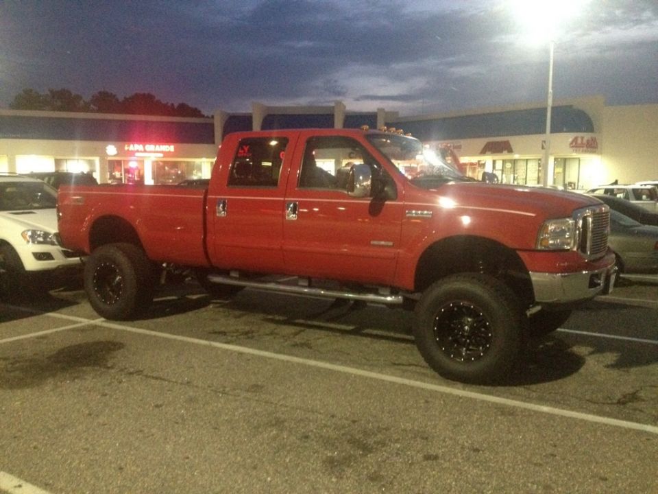 Red crew cab pickup truck parked in a lot. It has large tires and running boards