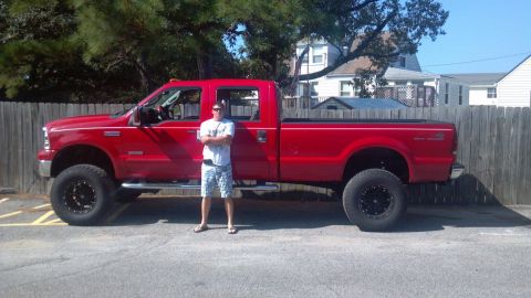 2007 Ford F-350 - A man stands beside a bright red 2007 Ford F-350 Super Duty pickup truck with custom wheels and a lifted suspension.