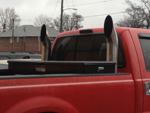 2007 Ford F-350 - A red pickup truck is shown from the rear with large chrome exhaust stacks and a black toolbox.