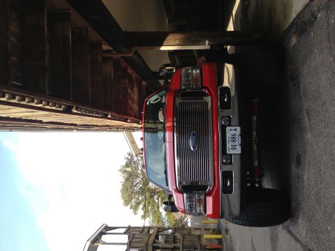 2007 Ford F-350 - A red 2007 Ford F-350 is parked head-on under a wooden overhang.