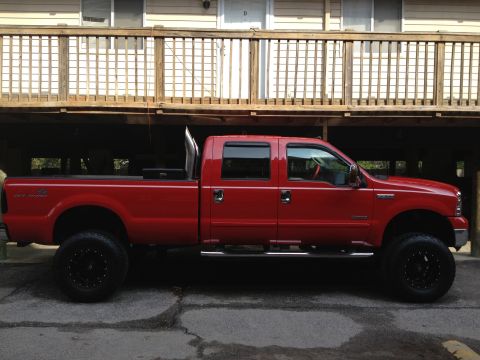 2007 Ford F-350 - This lifted red 2007 Ford F-350 pickup truck features a prominent exhaust stack and aggressive off-road tires.