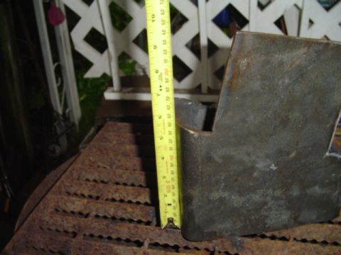 1993 Ford Bronco - A metal bracket is measured with a tape measure, with a rusty grate visible in the foreground.