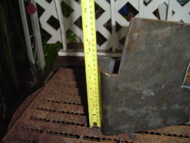 Rusty metal bracket next to a yellow tape measure, with a white lattice fence in the background
