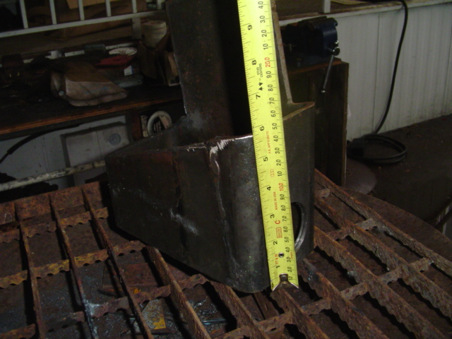 Dark metal radius arm bracket with yellow measuring tape showing approximately 6 inches