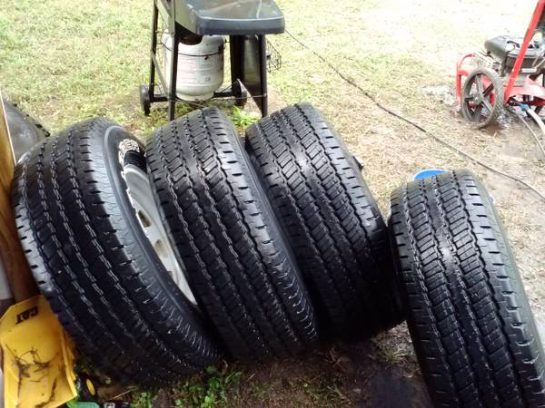 Four tires leaning against each other on wet ground, with a grill and pressure washer in the background