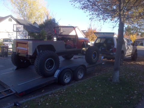 1985 Jeep CJ7 - Modified 1985 Jeep CJ7 pickup conversion loaded onto a trailer, with a pickup truck in the background.