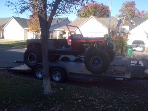 1985 Jeep CJ7 - A heavily modified off-road vehicle is being transported on a trailer, its custom suspension and large tires.