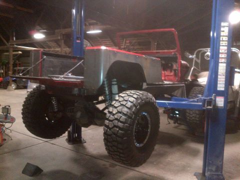 1985 Jeep CJ7 - A modified Jeep CJ-series is raised on a hydraulic lift inside a garage, undergoing custom fabrication.