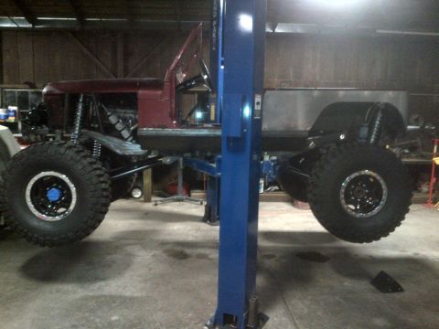1985 Jeep CJ7 - This heavily modified off-road vehicle is elevated on a lift, its large tires and custom suspension.