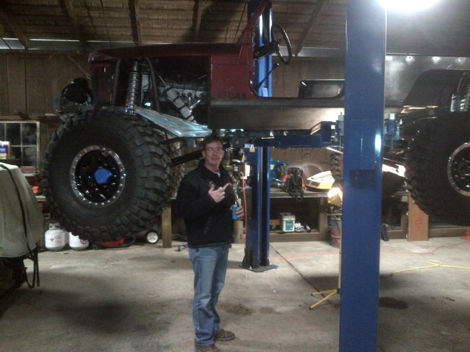 Modified Jeep body on a lift with oversized tires, a man stands beside it