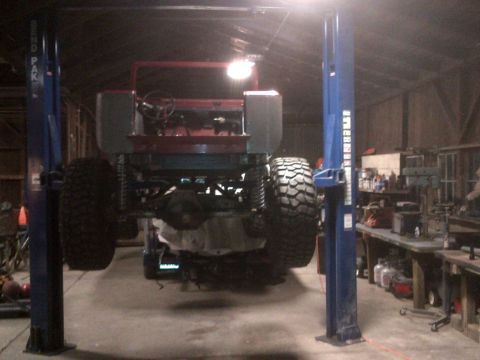 1985 Jeep CJ7 - 1985 Jeep CJ7 undergoing work on a vehicle lift, showing its rear end and large off-road tires.