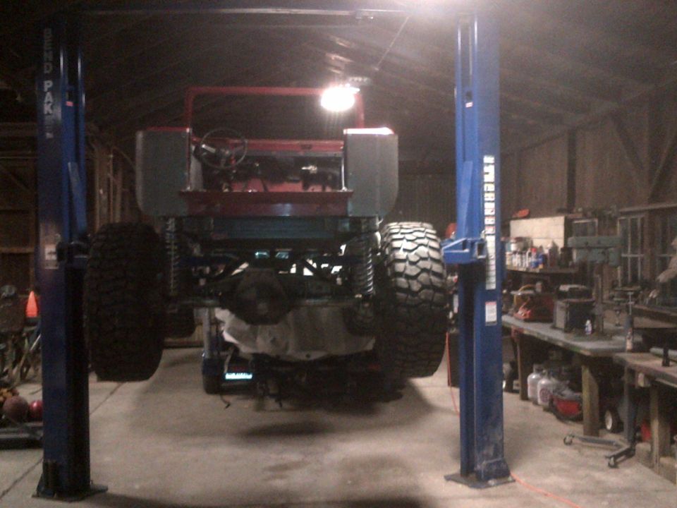 Red Jeep CJ-series on lift, rear view, large tires