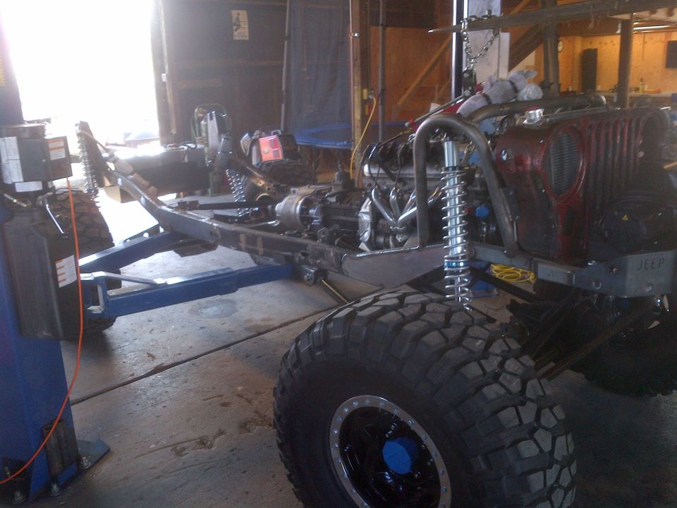 1985 Jeep CJ7 frame with engine and suspension components visible, in a garage