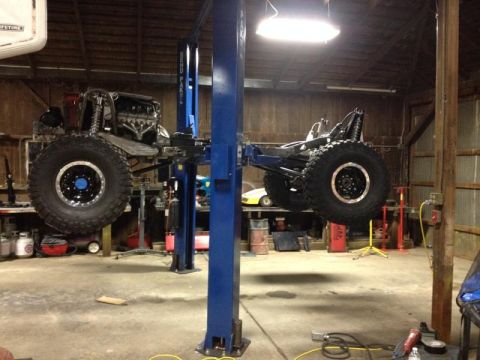 1985 Jeep CJ7 - This vehicle's chassis and large tires are visible while it is elevated on a lift in a workshop.