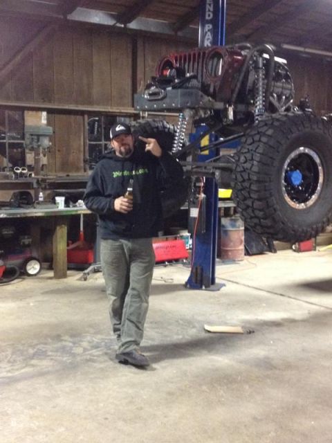 1985 Jeep CJ7 - A man stands in a workshop next to a custom Jeep being worked on in a lift.