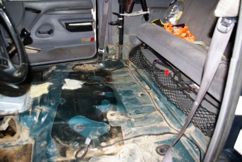 1995 Ford Bronco - The interior of a vehicle is shown with the floor removed, exposing the transmission tunnel and various components underneath.