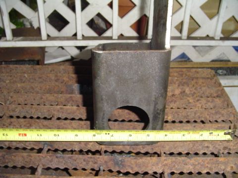 1993 Ford Bronco - A short section of square steel tubing with a large round hole bored through one face stands on a rusty grate, with a yellow tape measure l…
