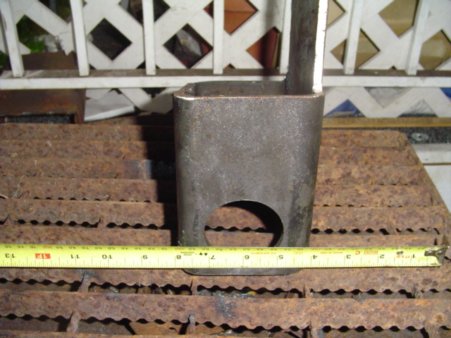Square steel tube with bored hole measured against a yellow tape measure