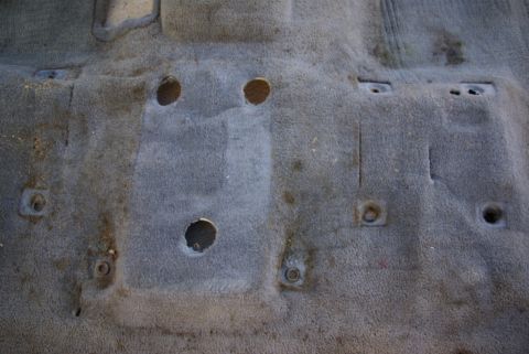 1995 Ford Bronco - The worn carpet of a vehicle interior shows holes and mounting hardware.