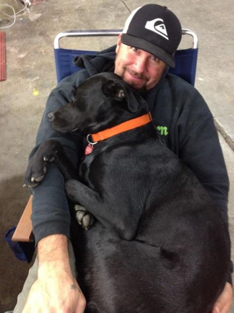 1985 Jeep CJ7 - A man embraces his black dog while sitting in a chair indoors.