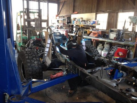 1985 Jeep CJ7 - A person welds a vehicle frame in a workshop, with a forklift visible in the background.