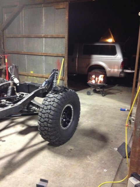 1985 Jeep CJ7 - A Jeep CJ frame and large tire are in the foreground, with a silver pickup truck visible in the background.