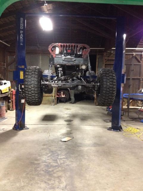 1985 Jeep CJ7 - Jeep CJ7 body undergoing work on a lift, showing its front end and large tires.