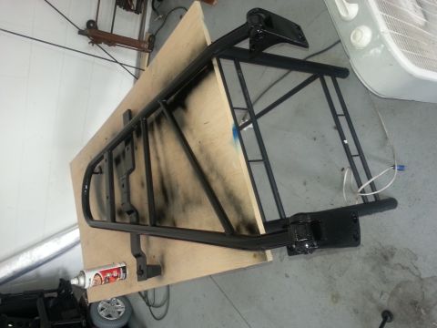 1994 Ford Bronco - A black metal rack, possibly for a vehicle, is shown on a piece of plywood with spray paint.