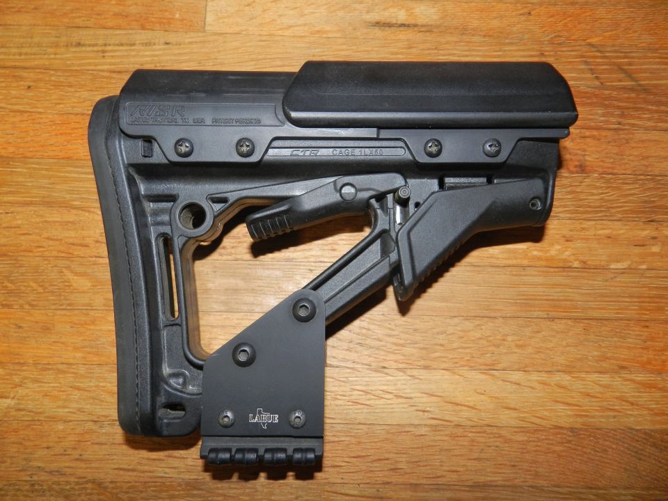 Black adjustable gun stock with visible text and mounting hardware on a wooden surface