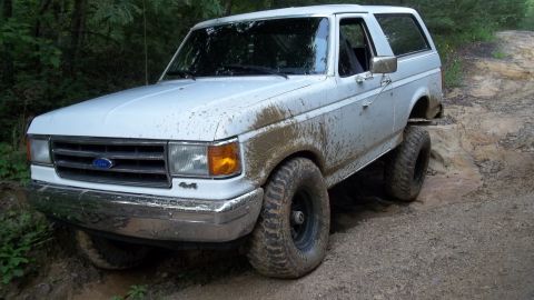 1990 Ford Bronco - A white 1990 Ford Bronco navigates a muddy off-road trail.