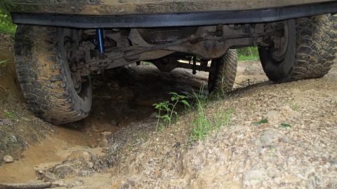 1990 Ford Bronco - The undercarriage and tires of an off-road vehicle are visible as it navigates a rough terrain.