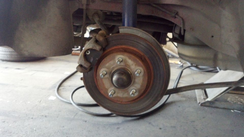 close-up of a rusty car brake rotor and caliper assembly, with a tire visible in the background