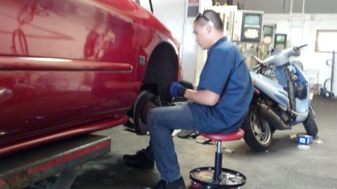 1996 Ford Taurus - Mechanic works on the wheel well of a red car, with a scooter visible in the background.